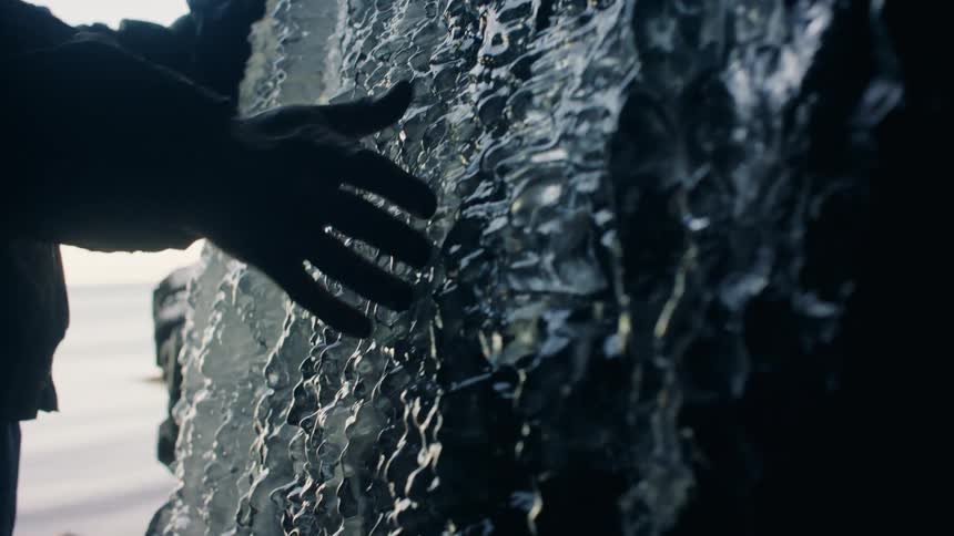 A persons hand with gloves passing over the surface of a very rough rock