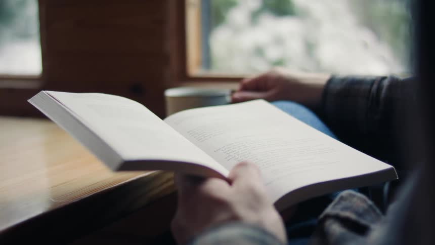 Someone reading a book while drinking from a metal mug