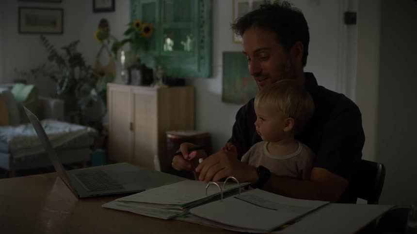 A clip of a man baby sitting while working on his laptop