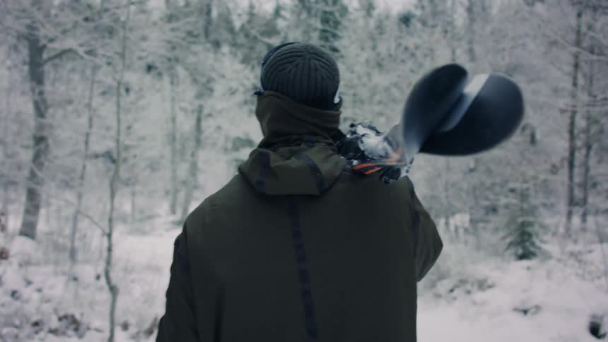 Male skier carries skis on his shoulder while walking through frozen woods during winter