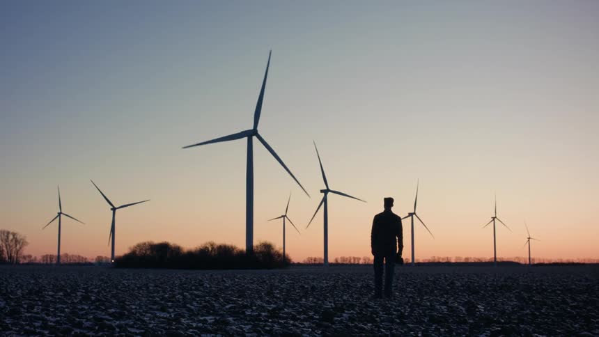 A person watching wind farms rotating during sunset