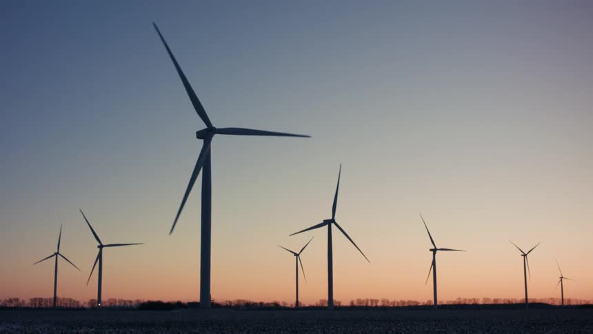 Wind turbines turn slowly during winter against a red tinted horizon