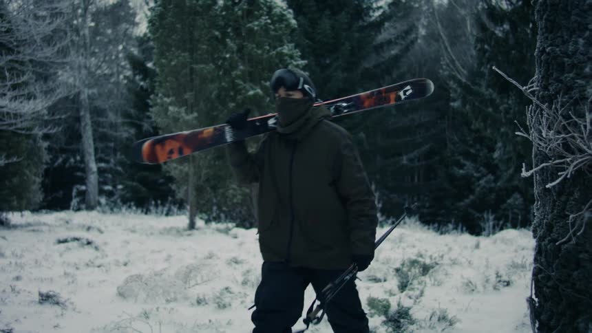 A man is walking in a snowy region in a forest and with a ski board on his shoulder