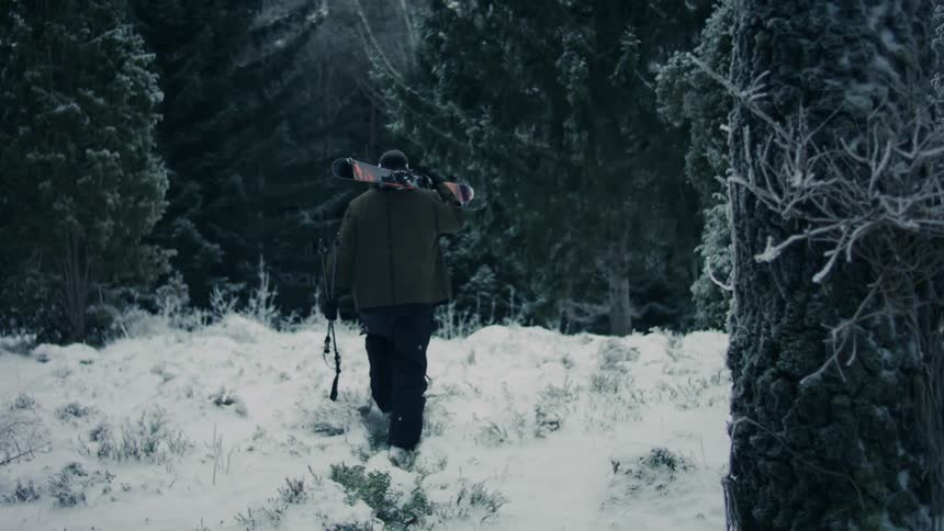 A person carrying a snowboard in the snowcovered forest