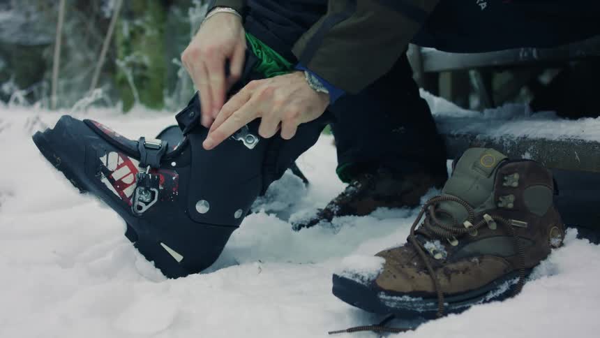 A person is putting a boot on his foot and the ground is covered in snow