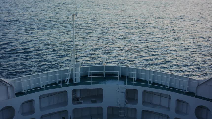 Bow of a ship sailing across the ocean at sunset