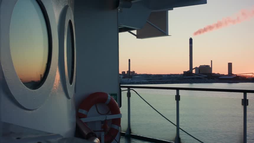 A smokestack on an industrial area seen from a ship at sunset