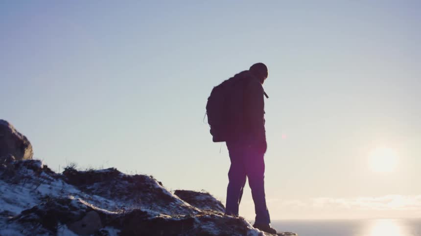 Man trekking through a snowy mountain towards the sea with the morning sun reflecting on the horizon