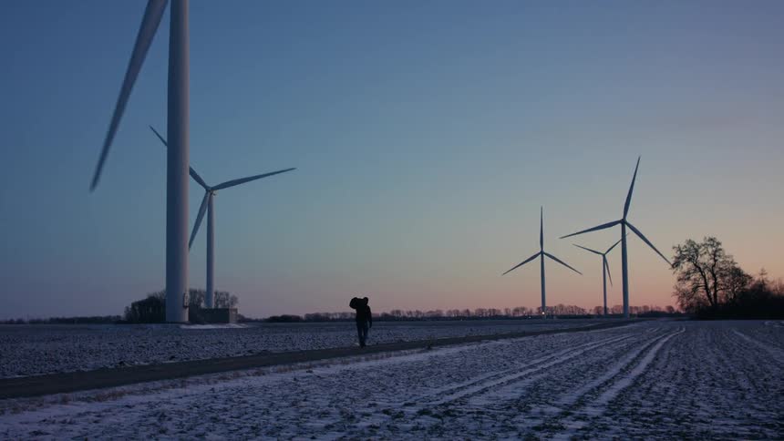Man walking in a snowcovered grassland amid wind turbines against a morning sky