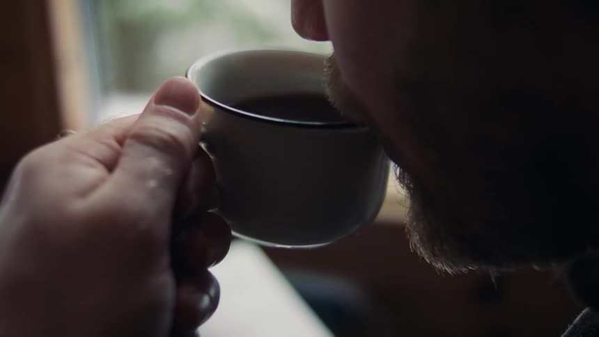 Older man sits near window drinking coffee and reading a book