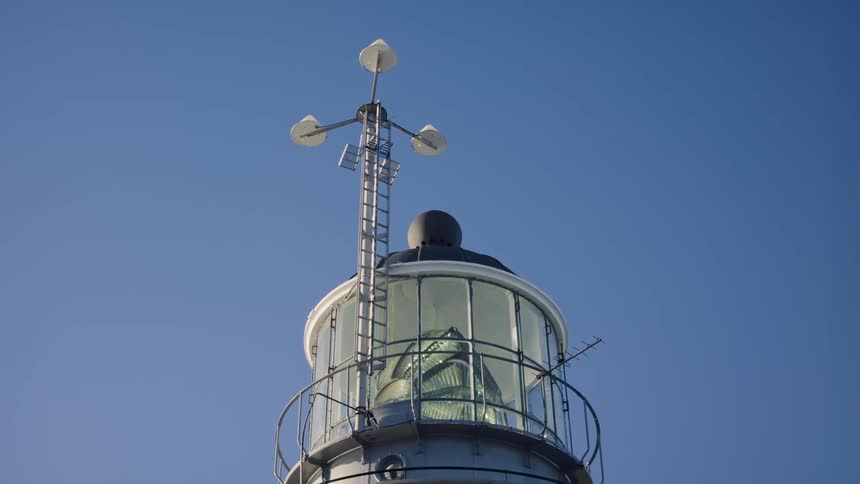 A lighthouse that has its lantern rotating and its a day with a very blue sky