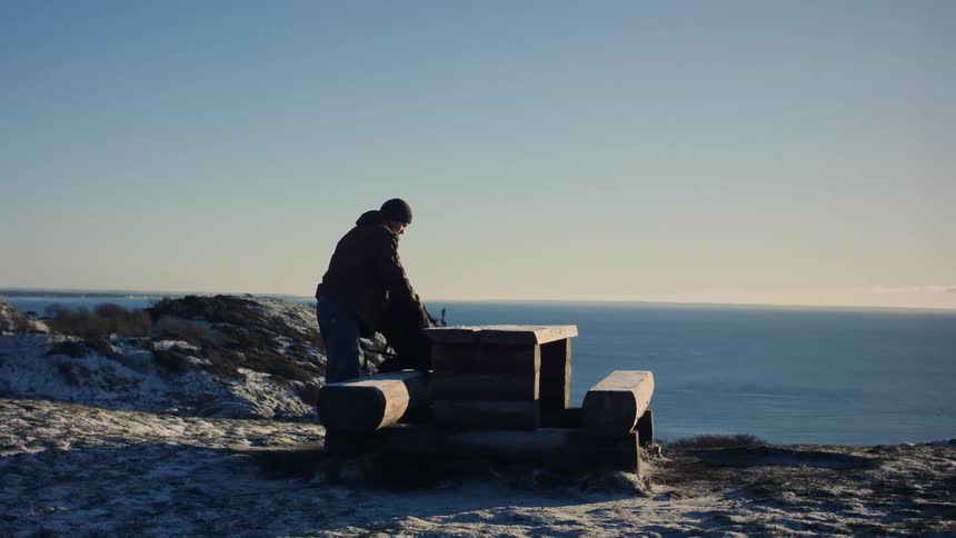 A hiker sets his backpack in a public picnic bench then sits on it