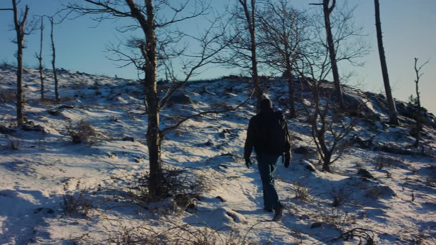 Hiker carrying a backpack walking on the hills covered in snow at morning