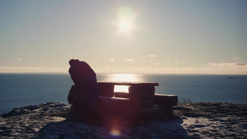 A person sitting on a wooden bench on a coastal hill