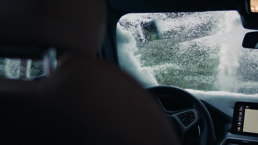A person uses an ice scraper to clear the windshield of their vehicle