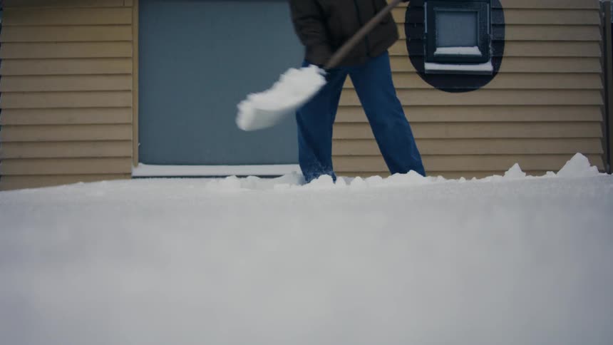 Man with a shovel clearing snow in front of a house entrance