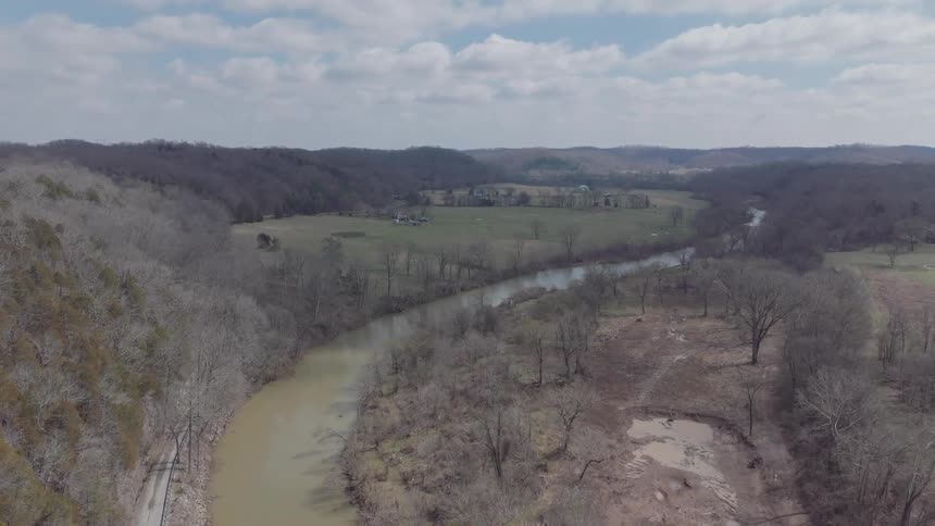 Buildings spread through field between hills and river winding by leafless woods