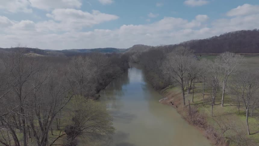 A river with still water and several trees beside it that are leafless