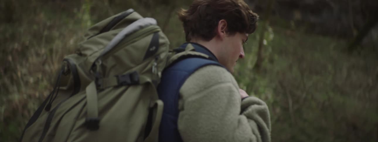 Backpacker hikes through woods at base of slope