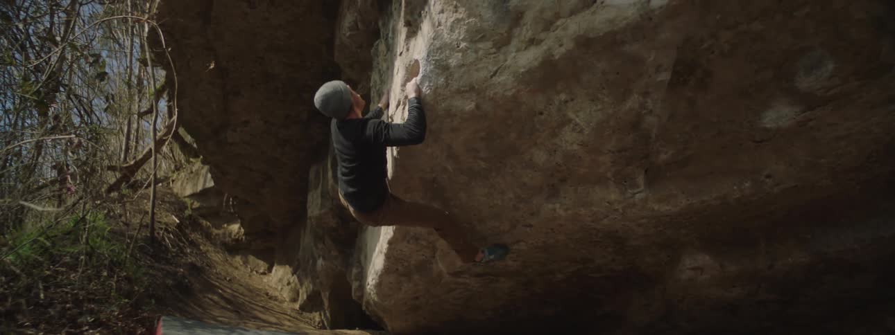 A man with a cap is climbing a rock