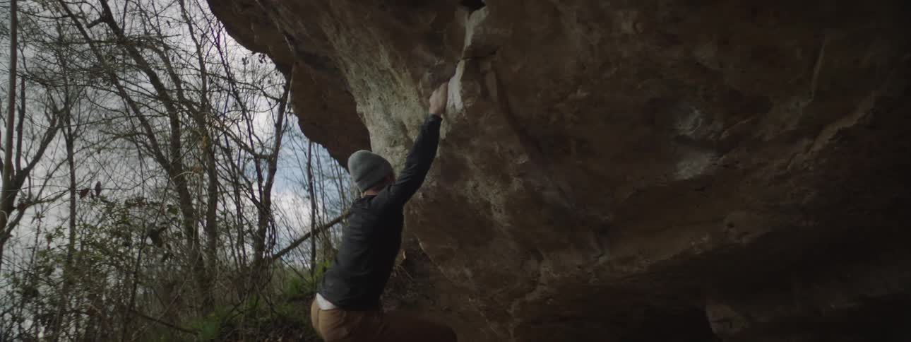 A man tries to maintain his footing while rock climbing in a forest