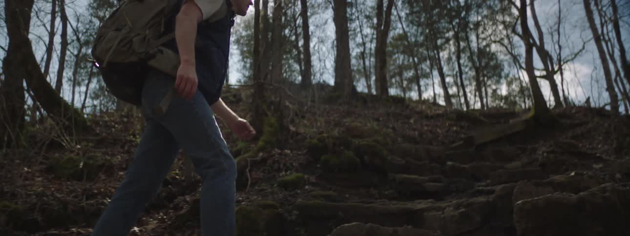 Backpacker walks up forest trail on steep slope on a sunny day