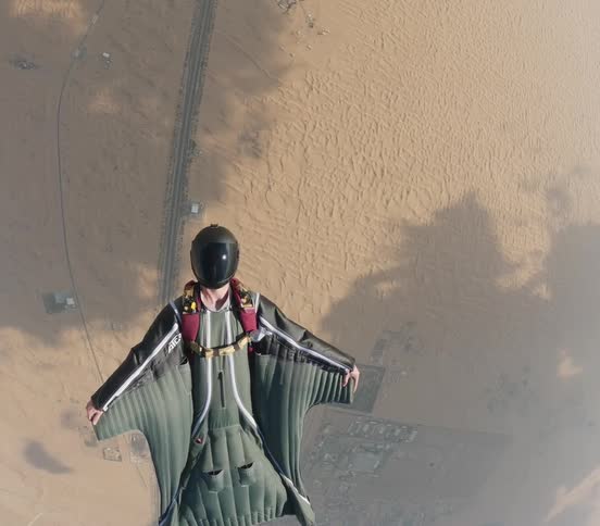 A person gliding towards the ground with a wing suit