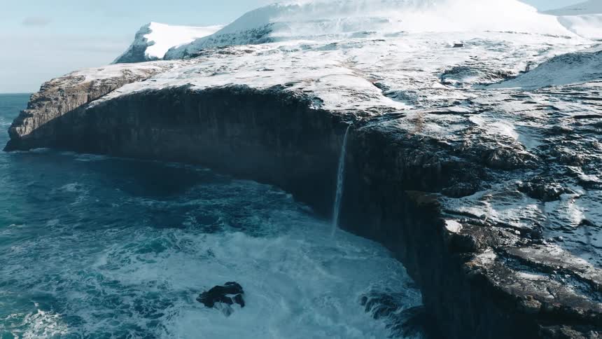 A small waterfall from a snowy land and the water falls into the sea