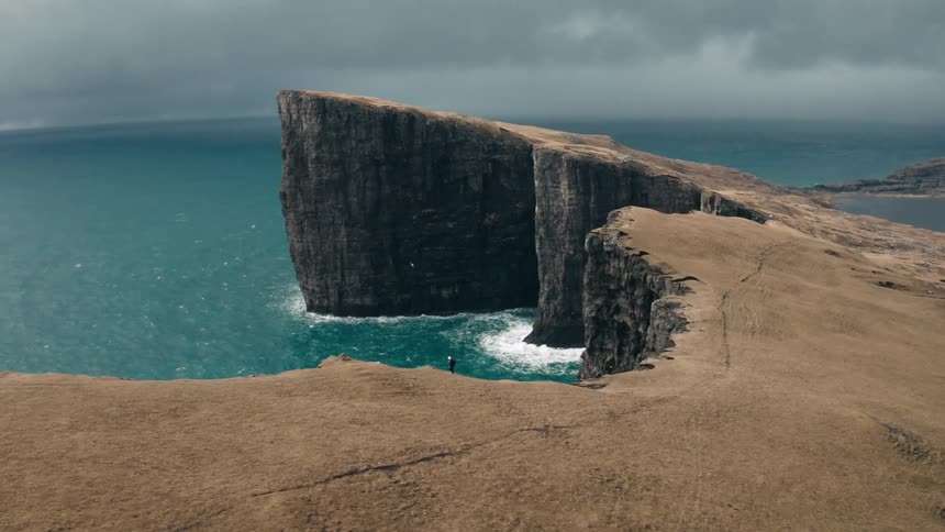 Hiker moves along seaside cliff as birds fly nearby on an overcast day
