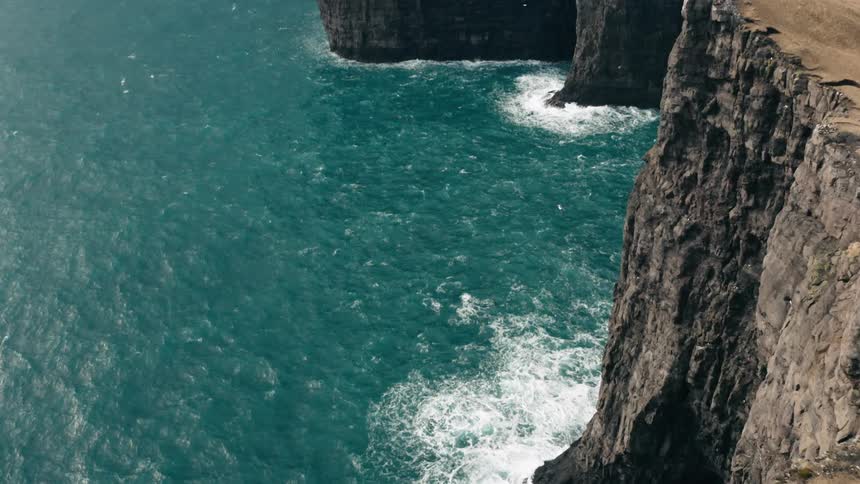 A hiker stands on the edge of a steep cliff overlooking the ocean on a cloudy day
