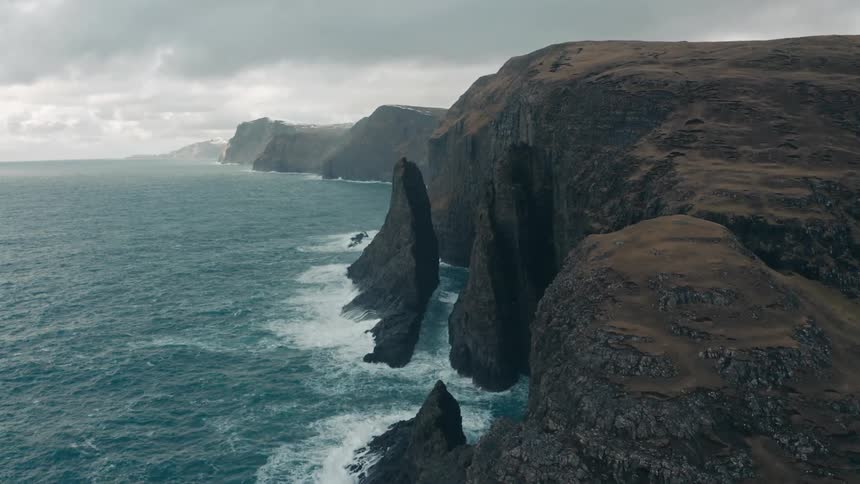 An aerial view of waves crashing against cliffs at the sea
