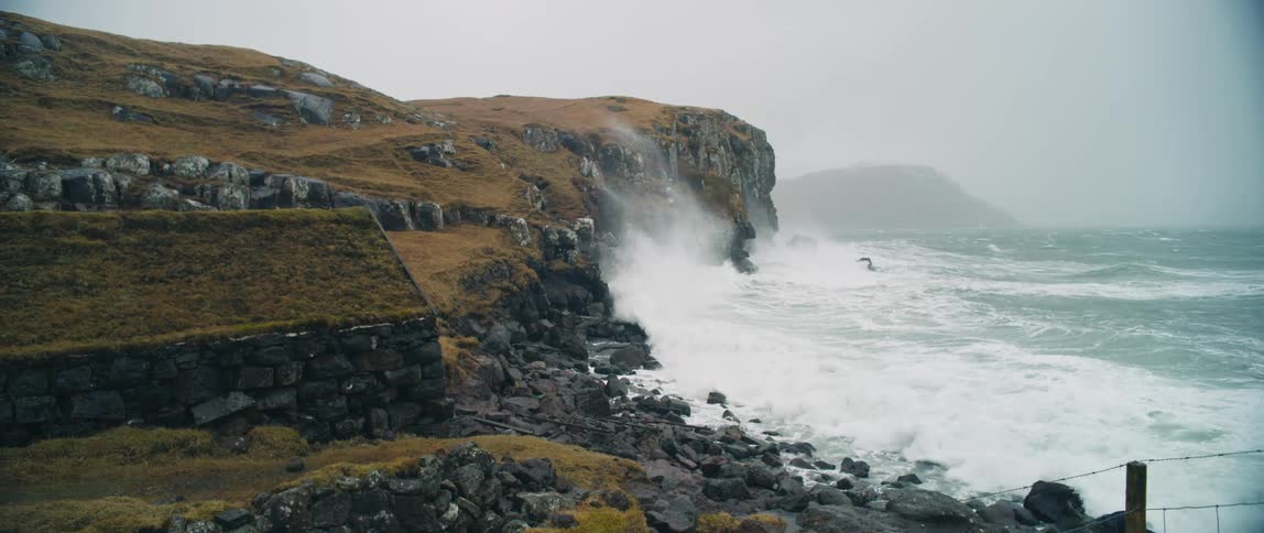Ocean waves crashing in the coastal cliffs near a stone house