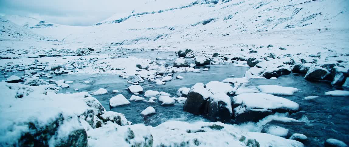 A stream with lots of rocks and the surrounding area is covered in snow
