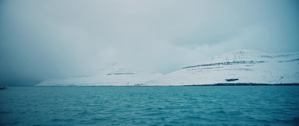 Snow covers mountainous coast under an overcast sky