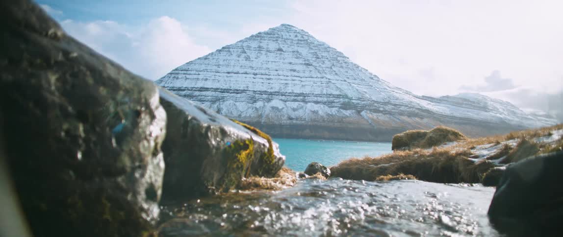 A river flowing towards the sea with a coastal mountain covered in snow