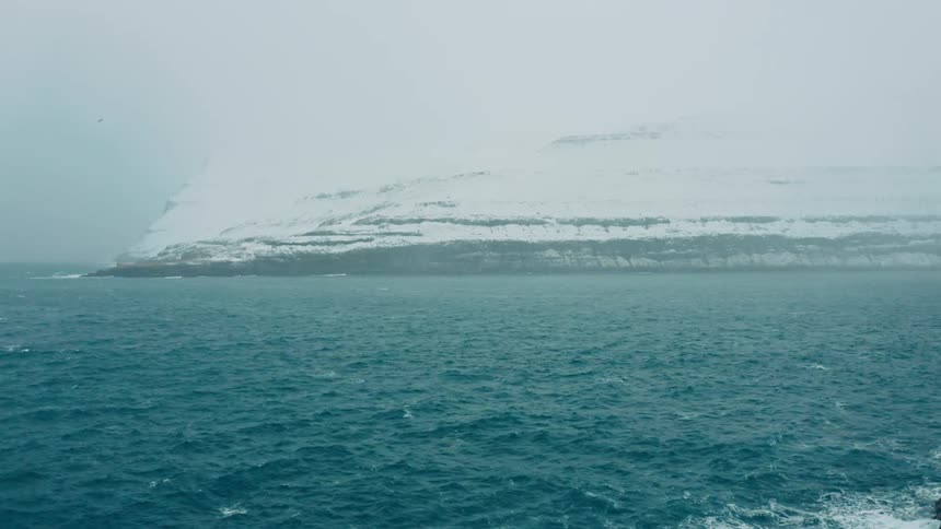A view of the ocean in the arctic with snow in the distance