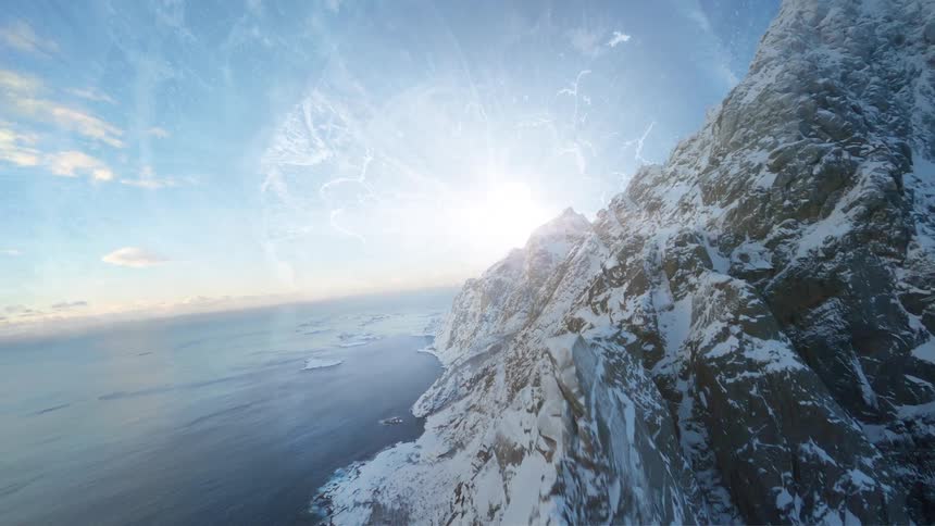 A huge stone mountain is covered with snow and there is an ocean around it