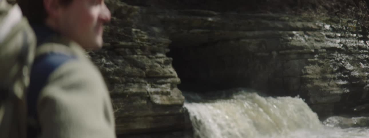 Man with a green backpack and a fleece watches a waterfall