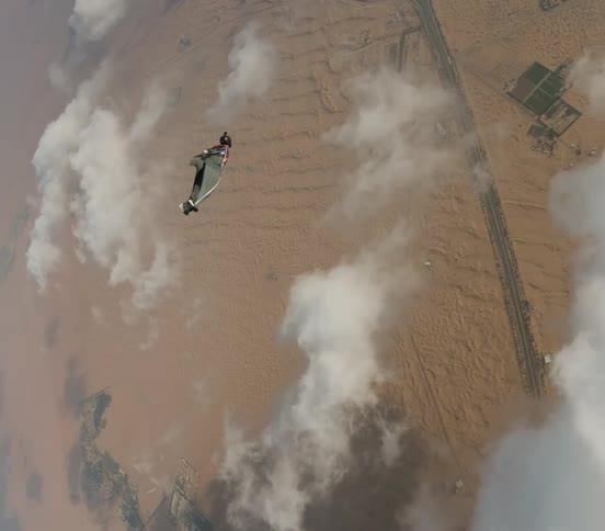 Someone wearing a wingsuit gliding in the sky towards the ground