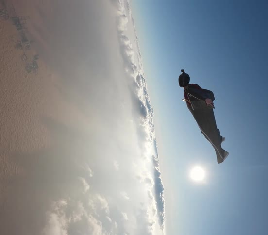 A person flying with a parachute in the sky with clouds during the day
