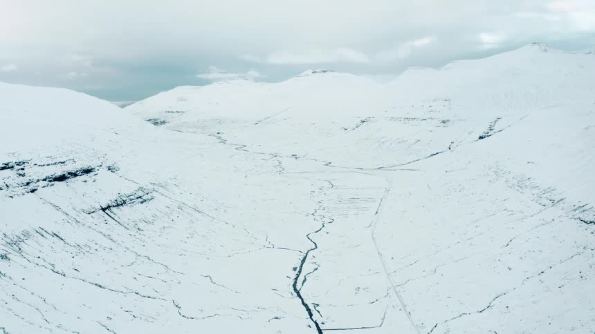 River flows through snow covered valley between mountains on an overcast day