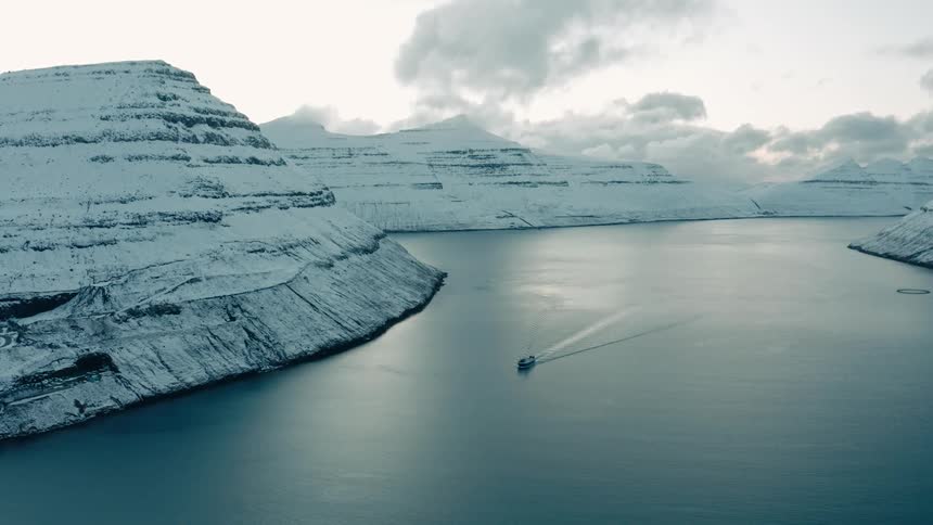 Snow covered mountains surround a lake with a boat driving in it