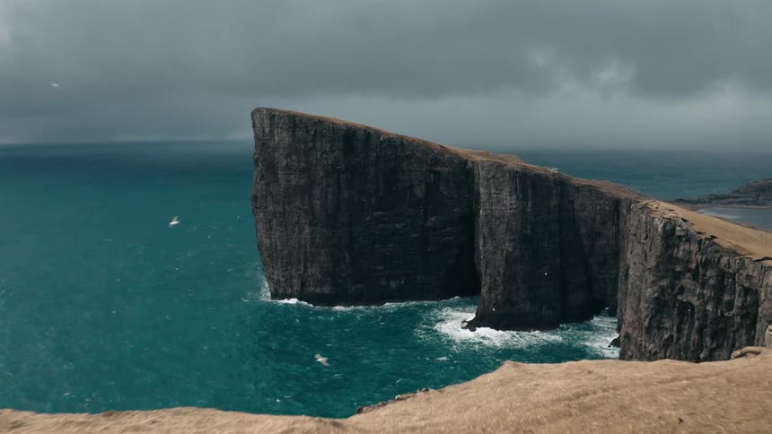 Backpacker hikes near edge of seaside cliff under dark clouds