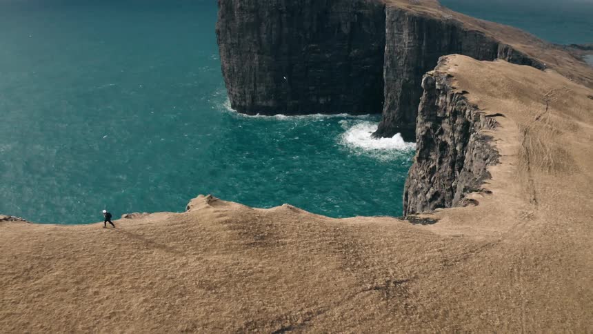 A hiker walking along the edge of a cliff over the ocean