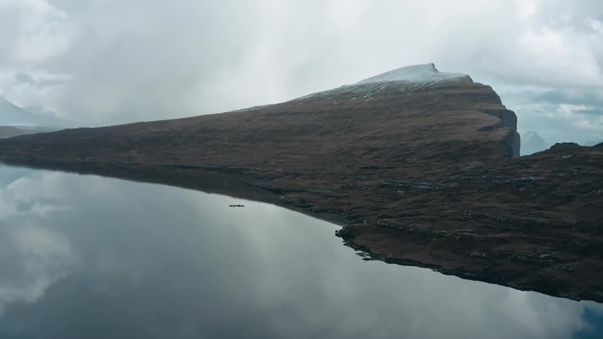 Panorama of a mountain by the ocean with reflective water under cloudy skies