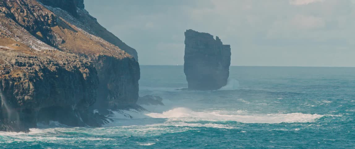 Waves break on the edge of the rock formation in the middle of the sea
