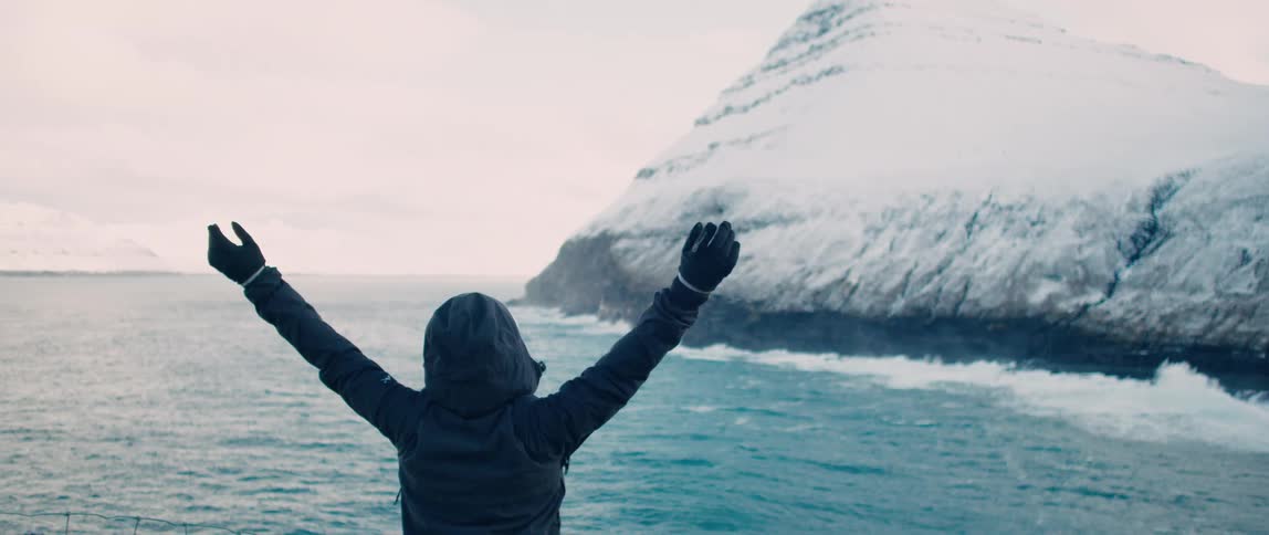 A woman throws her arms in the air in awe when she sees a glacier