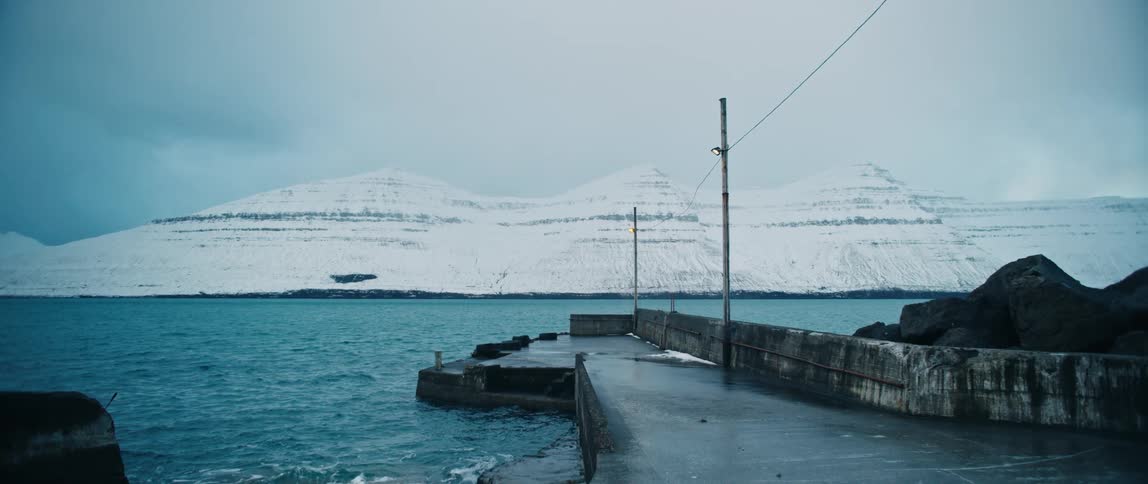 A pier in the sea and in the background several snowcovered mountains