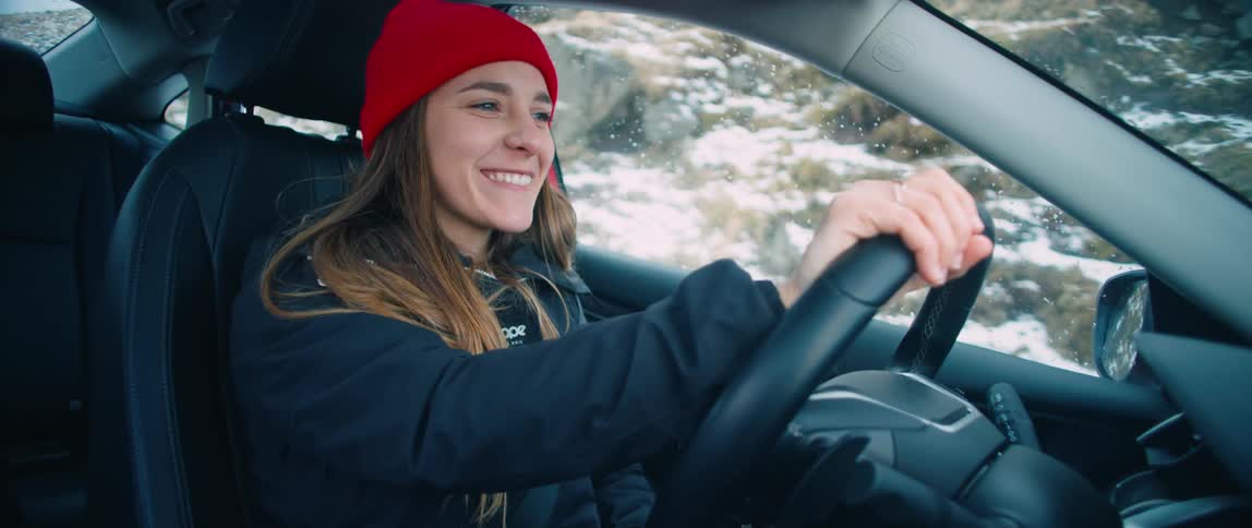 Woman smiles while driving past snow covered mountain side