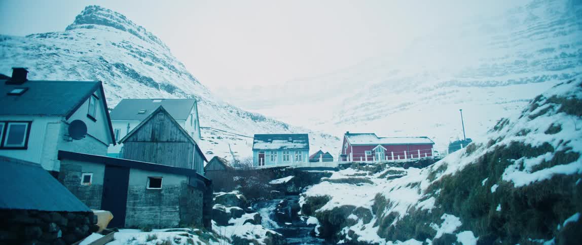 Houses in a snowy village with snowcovered mountains behind on a cloudy day